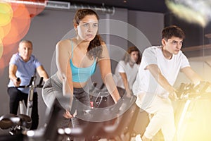 Man and woman taking indoor cycling class at fitness center, doing cardio riding bike