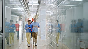 Man and woman talking in office. Colleagues walking with digital devices indoors