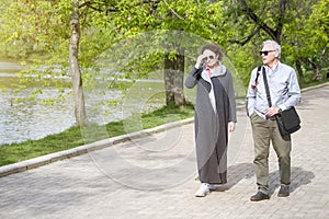 A man and a woman talking are walking along a pond in the park. Sunny spring day