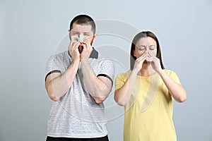 Man and woman with tissues suffering from runny nose on light grey background