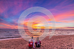 Man and woman together relaxing on sand beach romantic sky at sunset. Real people getting away from it all. Dramatic clouds over