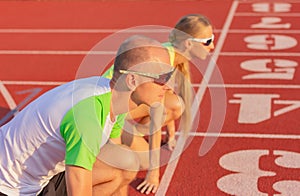 A man and a woman on the track of the stadium are preparing start of the race. side view, man in the foreground