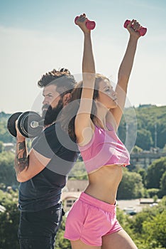 Man and woman training with dumbbells, athletic sport couple exercise outdoor. Fitness sexy models pumping up arm with