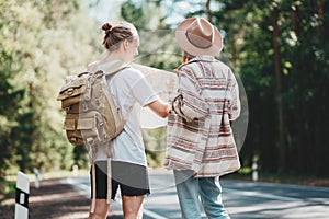 Man and woman traveling together and hold in hands location map and searching directional among trees in forest