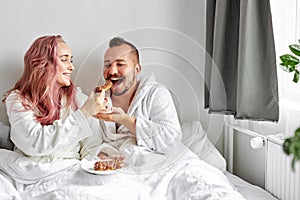 Man and woman treat each other with eclairs on bed