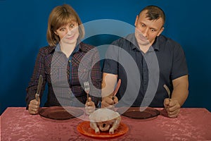 Man and the woman try to eat crude food. They sit at a table with a knife and a fork and plug