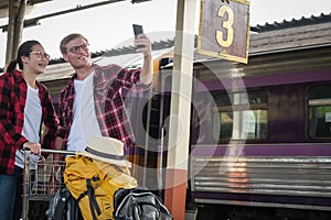 man & woman use smart phone to take selfie photo at train station. traveler couple travel together on holiday