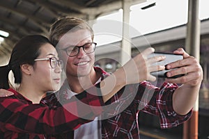 man & woman use smart phone to take selfie photo at train station. traveler couple travel together on holiday