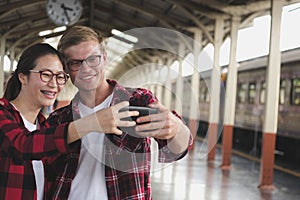 man & woman use smart phone to take selfie photo at train station. traveler couple travel together on holiday