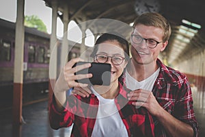 man & woman use smart phone to take selfie photo at train station. traveler couple travel together on holiday