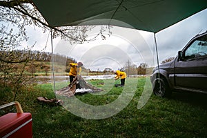 Man and woman on vacation in wilderness. preparing the camp, setting up the tent and folding chairs. Yellow raincoats from bad