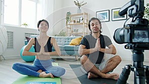 Man and woman vloggers meditating then showing follow me sign and doing high-five sitting on yoga mats