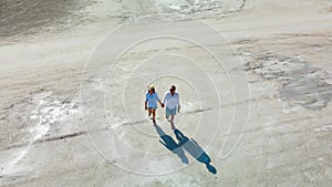 A man and a woman walk along a dry salt lake. Drone view of a guy and a girl.