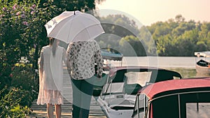 A man and a woman walk along the promenade and communicate. A man holds a white umbrella from the sun. Young couple