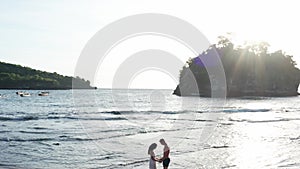 Man and Woman Walking Along Tropical Beach at Sunset, Tracking aerial shot of young couple on vacation having fun on the