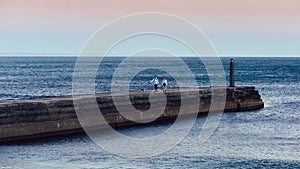 Man and woman walking dogs on a pier at sunset in Cascais, Portugal