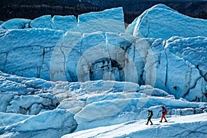 Man and woman walking narrow ridge on the Matanuska Glacier in Remote Alaska. Large crevasses and fins break up the ice all around