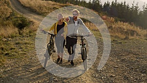 Man and woman walking on path with bicycles. Friends talking during walk