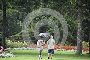 A man and woman walking in rain in a park.