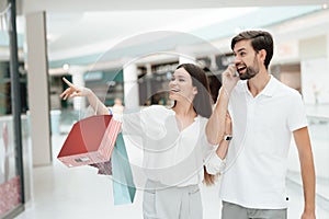 Man and woman are walking to another store in shopping mall. Man is talking on phone.
