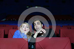 Man and woman watch movie and very much afraid in movie theater.