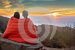 Man and woman watch sunset in blanket