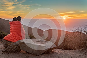 Man and woman Watch Sunset while under sleeping bag