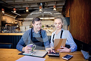 Man and woman wearing apron doing accounts after hours in a small restaurant. Employees checking monthly reports