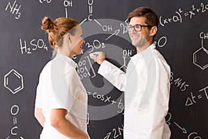 Man and woman wearing labcoats standing in front of a blackboard