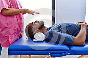 Man and woman wearing physiotherapist uniform having reiki session at physiotherpy clinic