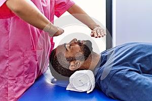 Man and woman wearing physiotherapist uniform having reiki session at physiotherpy clinic