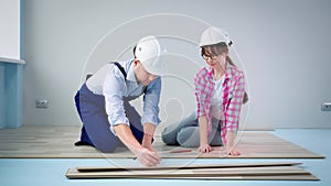 man and woman wearing protective helmets doing construction work and laying laminate flooring in new apartments