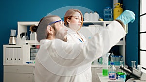 Man and woman wearing sciencist uniform holding test tubes at laboratory