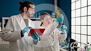 Man and woman wearing sciencist uniform using touchpad at laboratory