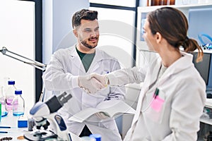 Man and woman wearing scientist uniform shake hands at laboratory