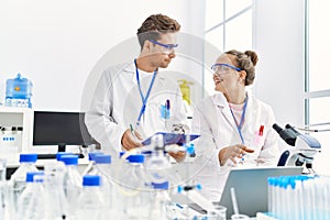 Man and woman wearing scientist uniform using laptop working at laboratory