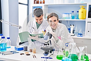 Man and woman wearing scientist uniform using microscope writing on notebook at laboratory