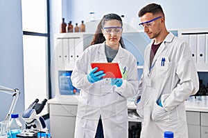 Man and woman wearing scientist uniform using touchpad at laboratory