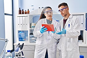 Man and woman wearing scientist uniform using touchpad at laboratory