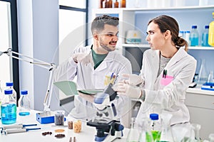 Man and woman wearing scientist uniform writing on notebook at laboratory