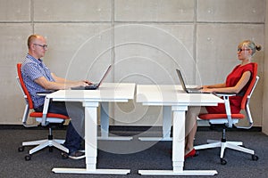 Man and woman working in correct sitting posture with laptops at desks in office