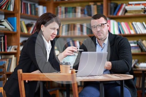 Man and woman working with laptop sitting in modern stylish room with bookshelves on background in library or bookstore