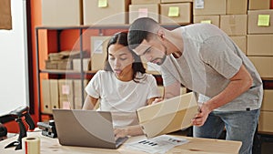 Man and woman working together, two office workers reading package information on laptop in the warehouse