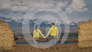 Man and woman in yellow green sportswear. Lovely couple of travelers hug and kiss near old stone enjoying highland