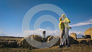 Man and woman in yellow green sportswear. Lovely couple of travelers hug and kiss near old stone enjoying highland