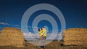 Man and woman in yellow green sportswear. Lovely couple of travelers hug and kiss near old stone enjoying highland