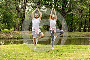 Man and Woman Yoga posture exercise in public garden park in summer