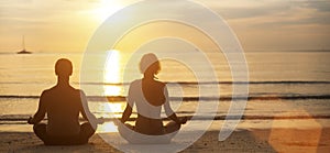 Man and woman yoga silhouettes meditating on Sea coast.