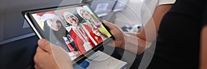 Man and woman celebrating christmas with friends in santa claus hats through screen on digital tablet in aircraft cabin