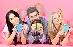 Man and women in domestic clothes, pajamas. Man and women, friends on happy faces lay, pink background. Threesome relax